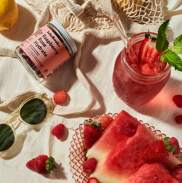 A cold glass of raspberry tea beside a plate of watermelon and strawberries.